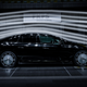 A black electric sedan with gaudy, gigantic wheels sits in a wind tunnel being sleek.